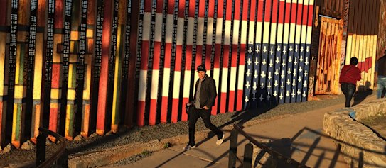 People pass graffiti along the border between the US and Mexico in Tijuana.