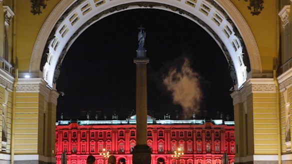 People walk past the Winter Palace in St Petersburg, illuminated in red for the upcoming 100th anniversary of the Bolshevik revolution.