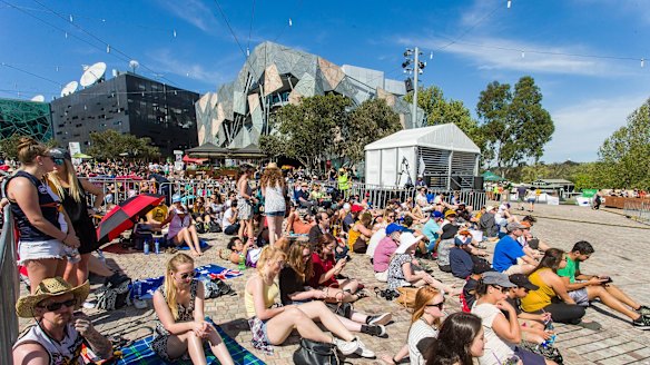 Fans settle in at Federation Square to watch the grand final in the sun.