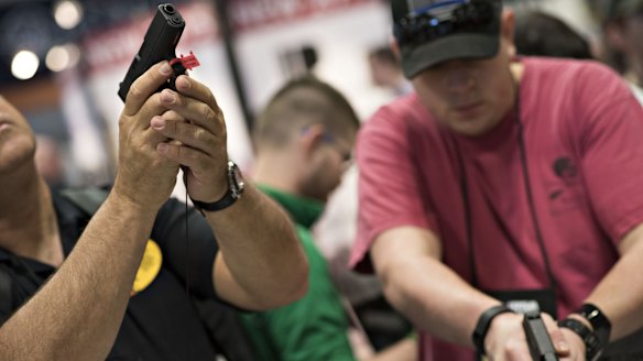 Attendees look over pistols on display at the NRA convention in April in Nashville. 