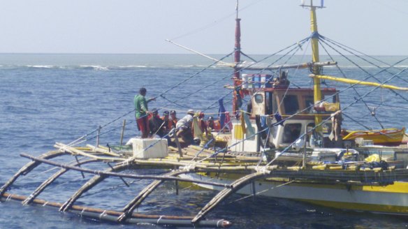 Chinese Coast Guard officers, to the rear, approach Filipino fishermen on their boat on Scarborough Shoal last year. 