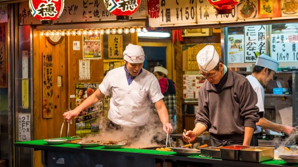 Street food vendors cooking takoyaki in Osaka, Japan.