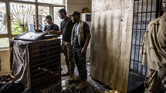 Iraqi security forces look at literature found on top of a small cage that the Islamic State used to hold prisoners in the Nazal district of Fallujah.