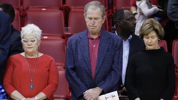Former president George W Bush observes a moment of silence with his wife, Laura Bush (right), and others in support of the victims of the Paris terrorist attacks, before a college basketball game.
