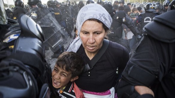 A woman and child flee as police respond with force against migrants protesting on the Serbia-Hungary border after they pushed through the border fence into Hungary.