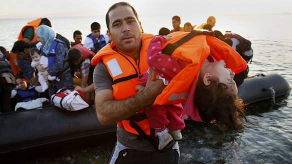 A Syrian refugee carries a child as they arrive at a beach on the Greek island of Kos after crossing the Aegean Sea from Turkey on a dinghy.