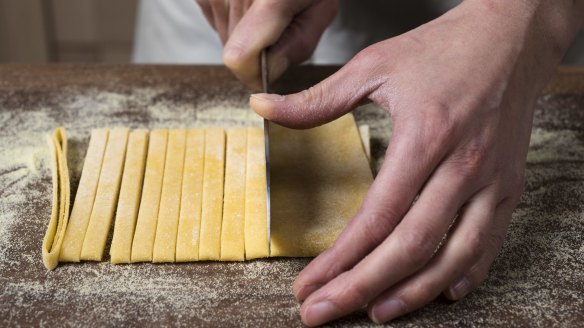 After folding pasta sheets into several layers, a knife is used to cut wide ribbons.