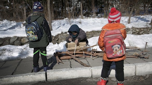 A woman ties wood she collected into a bundle as two children wait in Hyangsan county, North Pyongan, North Korea.