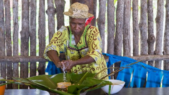 Kanak woman making bougna, wrapping protein in banana leaves with root vegetables, banana and coconut milk. 