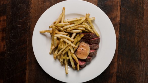 The bavette steak comes pink and glistening inside, and darkly crusty outside, smothered in skinny, skin-on fries.