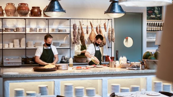 Industrial spotlights hang over a charcuterie-backed chef workspace at the new venue. 