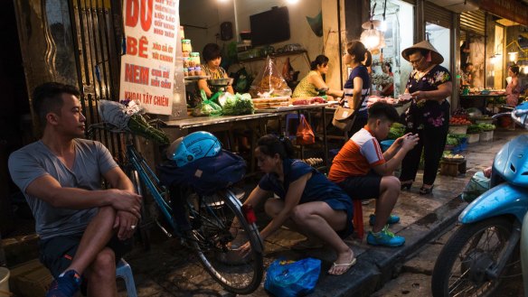 People use the sidewalk in front of a street vendor's shop in Hanoi. 