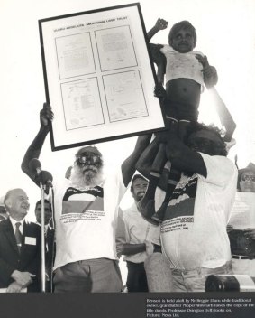 Vincent Nipper is held aloft as his grandfather, Nipper Winmati, raises the title deeds at the 1985 handback.