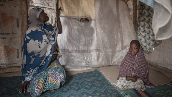 Hamsatu, 25, peeks through a tear in the divider of her tent while holding her one-year-old daughter Hauwa on her back, as she sits next to Fatima, three, at Dalori Internally Displaced Persons Camp in Maiduguri, Nigeria. 
