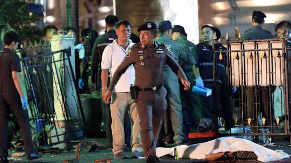 A police officer walks by the body of a victim covered in a white sheet following an explosion at the Ratchaprasong intersection in Bangkok.
