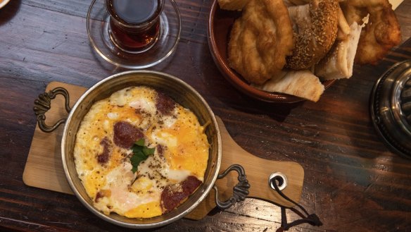Baked eggs with sucuk (spicy beef sausage) and bread is part of the breakfast spread.