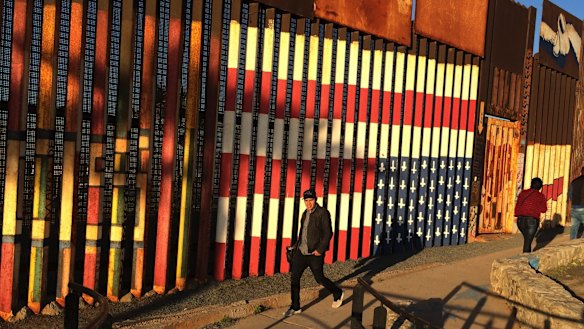 People pass graffiti along the border between the US and Mexico in Tijuana.
