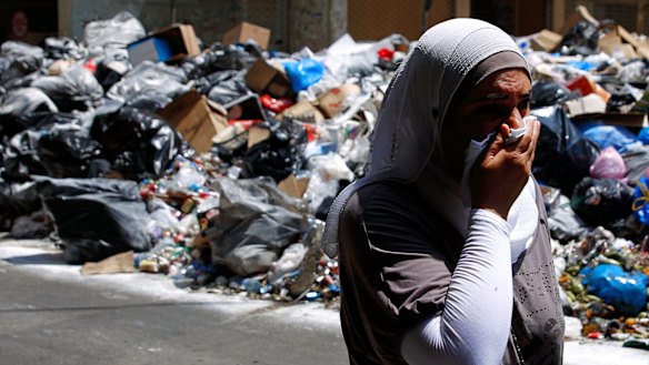 A Lebanese woman covers her nose from the smell as she walks on a street partly blocked by piles of garbage in Beirut on Monday. 