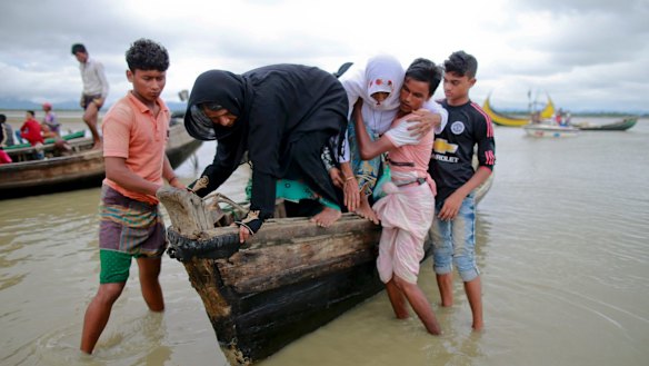 Bangladeshi villagers help two elderly Rohingya women get down from a boat after crossing a canal at Shah Porir Deep, in Teknak, Bangladesh