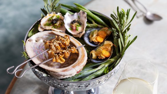 A mini seafood tower holding oysters with finger lime, barbecued abalone skewers and mussel escabeche.