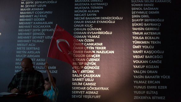 A young boy holds a Turkish flag in front of a board, at Taksim Square, listing the names of people killed during last week's failed coup attempt. The death toll now stands at 246 and 1536 wounded. 