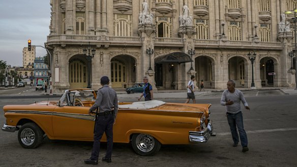 A driver hurries back to his car as a police officer stands next to it, in front of the Gran Teatro de La Habana Alicia Alonso, where President Barack Obama is scheduled to speak.