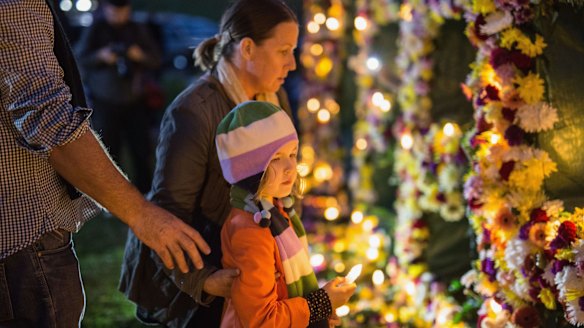 A young girl is guided to place a candle on a flower wall.