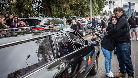 Mourners console eachother as the hearse passes Cleve Gardens in St Kilda.
