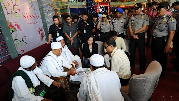 Police look on at a Surabaya shopping centre as centre staff sign a document promising not to dress employees in Christmas apparel.