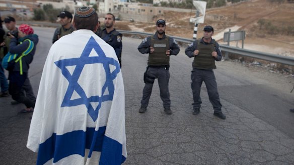 An Israeli settler draped in the country's flag stands next to Israeli police in a demonstration at the enterance to the  Palestinian village of Beit Sahur, in the occupied West Bank. 