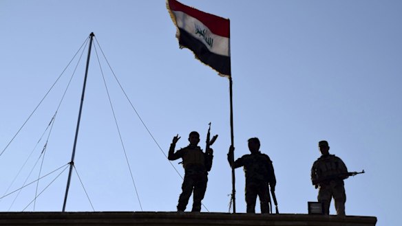 Iraqi soldiers plant the national flag over a government building in Ramadi.