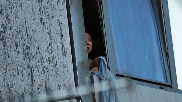 A resident peers out of a window from a small section of the building that was not on fire on Wednesday morning.