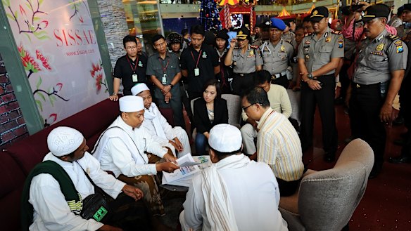 Police look on at a Surabaya shopping centre as centre staff sign a document provided by the Islam Defenders' Front promising not to dress employees in Christmas apparel.