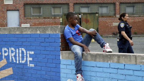 A boy sits on a wall as a Baltimore police officer walks by  near the site of unrest following the funeral of Freddie Gray. 