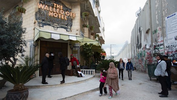 People pass the Walled Off Hotel and the wall in Bethlehem, in the Israeli-occupied West Bank.
