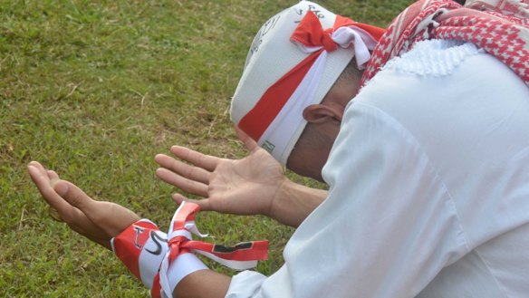 A man wearing Indonesian flag colours and Islamic symbols prays at an anti-Ahok rally.