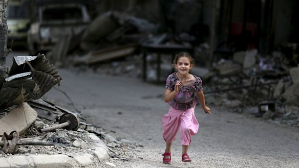 A girl runs near damaged buildings and debris in Jobar on Wednesday.