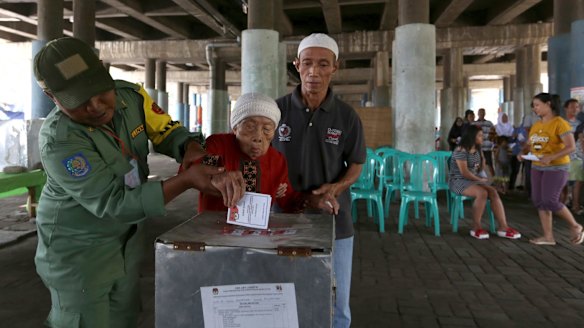 Electoral workers help an elderly woman cast her ballot at a makeshift polling station under a bridge.