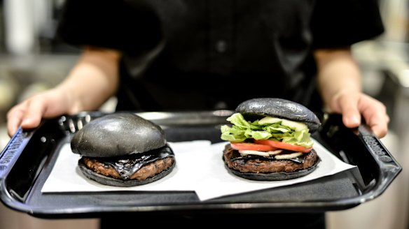 The Kuro Pearl, left, costs 480 yen and comes with black buns and cheese smoked with bamboo charcoal and black sauce made of squid ink. The Kuro Diamond, priced at 690 yen, also comes with lettuce, tomato, onion and mayonnaise.