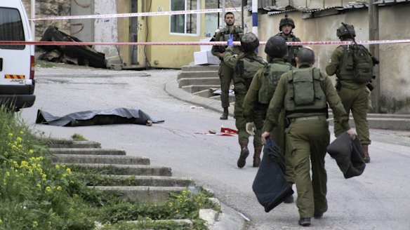 Israeli soldiers stand near the body of a Palestinian who was shot and killed by a soldier last week while laying wounded on the ground.
