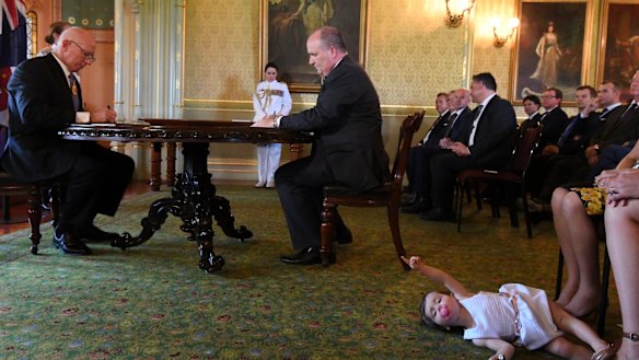 David Elliott, new Minister for Counter Terrorism, signs an oath at Government House as John Barilaro's daughter Sofia plays at her mother's feet.