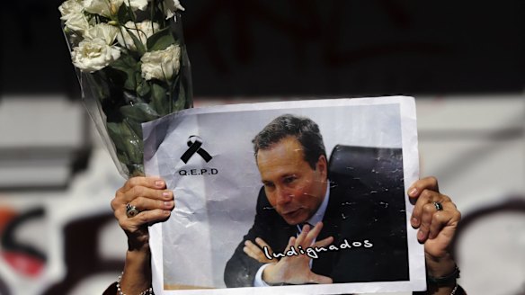 A woman holds up flowers and an image of late prosecutor Alberto Nisman while waiting for the hearse with his remains, in Buenos Aires January 29, 2015.