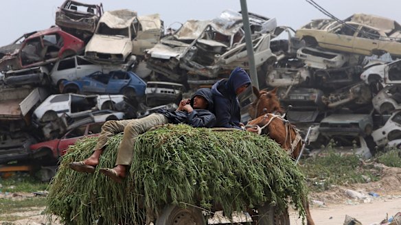 Farmers rest on a horse cart loaded with animal fodder as they pass a junkyard on their way to their barn, in  the Gaza Strip town of Beit Hanoun.