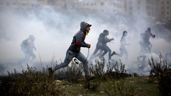 Palestinian protesters run for cover from tear gas fired by Israeli soldiers during clashes in Ramallah on Monday. 