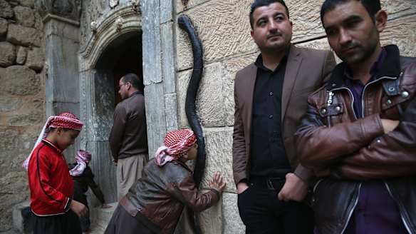 A Yazidi boy kisses a figure of a black snake at the entrance of the Temple of Lalish,in Nineveh Province, Iraq. 