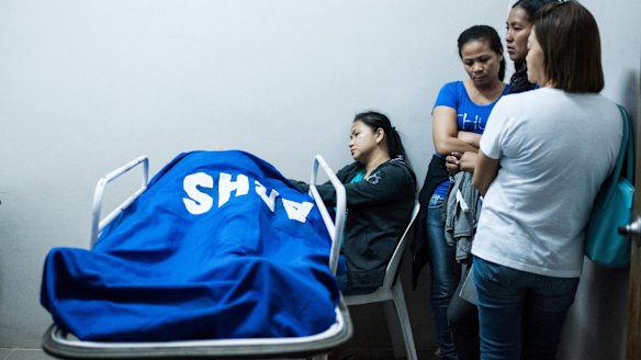 Relatives stand beside the body of a police intelligence officer killed during a botched drug raid which also killed three drug suspects on August 20.