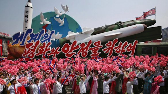 North Koreans wave as they march next to a float display of models of different missiles during a military parade in Pyongyang earlier this month.