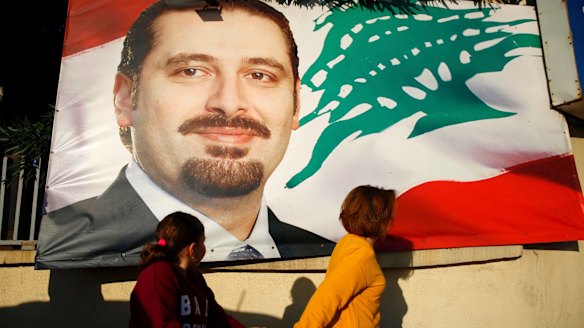 A woman and her daughter pass by a poster of outgoing Prime Minister Saad Hariri, in Beirut, Lebanon.