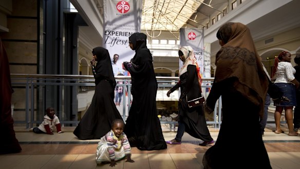 A young Kenyan girl and her brother play on the floor while other shoppers walk around the reopened Westgate Shopping Mall.