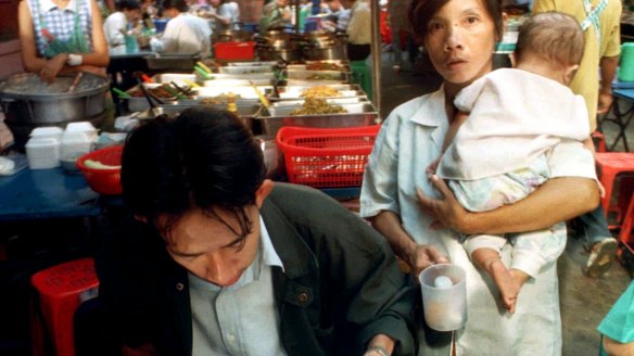 A woman begs for money or food from a diner while holding a baby in Bangkok.